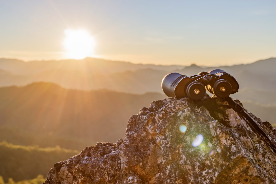 binoculars-on-top-of-rock-mountain-at-beautiful-sunset-background